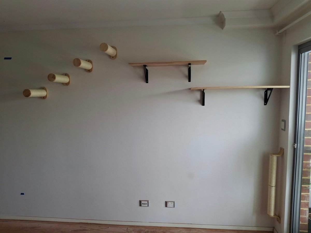 A finished cat climbing wall: four sisal steps rising to two pine shelves on black brackets, with a scratching post beside the balcony door