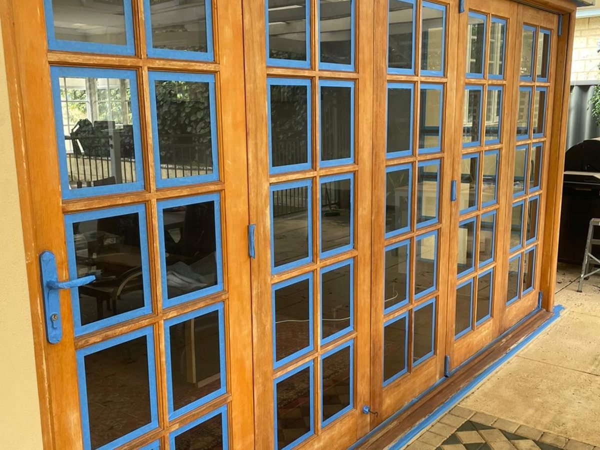 A run of solid timber French doors sanded back to bare timber, glass masked with tape, ready for staining